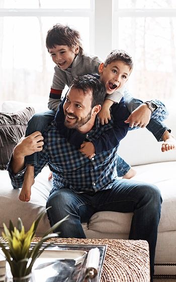 Father sitting on couch giving piggy back rides to his two sons