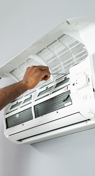 mans hand holding metal tool inside open wall air conditioner unit