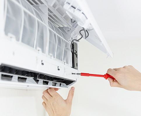 hand holding red screwdriver fixing open wall air conditioner